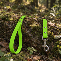 Biothane-Schleppleine mit Handschlaufe in Apfelgrün mit Edelstahl-Karabiner auf bemoostem Baumstamm im Wald