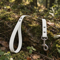 Biothane-Schleppleine mit Handschlaufe in Weiß mit Edelstahl-Karabiner auf bemoostem Baumstamm im Wald