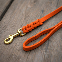 Detail: Fettlederleine in Orange auf Holzdielen, geflochtenes Ende mit Messingkarabiner und Handschlaufe