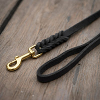 Detail: Fettlederleine in Schwarz auf Holzdielen, geflochtenes Ende mit Messingkarabiner und Handschlaufe