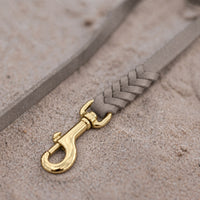 Detail: geflochtenes Ende mit Messingkarabiner an Fettlederleine in Grau auf Sand