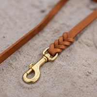 Detail: Messing-Karabiner und Flechtverbindung einer Fettlederleine in Cognac auf Sand
