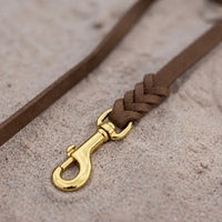 Detail: Messing-Karabiner und Flechtverbindung einer Fettlederleine in Braun auf Sand