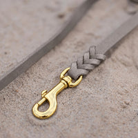 Detail: Messing-Karabiner und Flechtverbindung einer Fettlederleine in Grau auf Sand