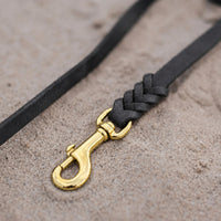 Detail: Messing-Karabiner und Flechtverbindung einer Fettlederleine in Schwarz auf Sand