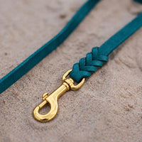 Detail: Messing-Karabiner und Flechtverbindung einer Fettlederleine in Türkis auf Sand