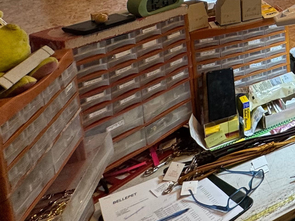 Sortierkästen mit Kleinteilen und beschrifteten Schubladen, davor fertige Lederleinen mit Messingkarabinern in Birtes Werkstatt