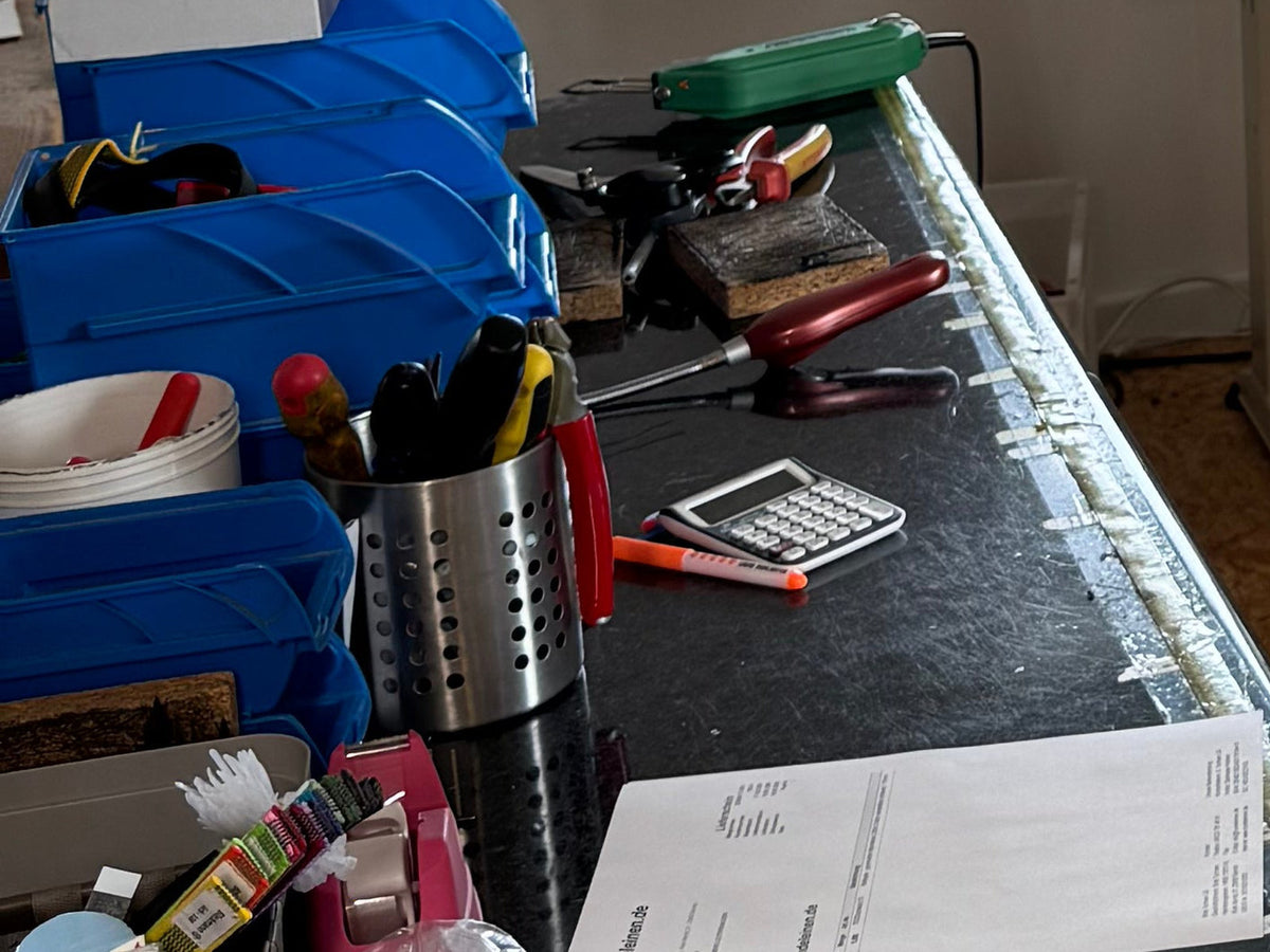 Zuschnitttisch in der Werkstatt mit Sattlerwerkzeug im Köcher, Zangen, Sichtboxen und Lieferscheinblock